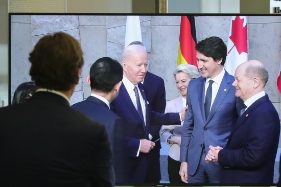 2022年3月24日，在比利時布魯塞爾的北約總部，一名男子觀看屏幕上美國總統(tǒng)拜登（右四）、歐盟委員會主席馮德萊恩（右三）、加拿大總理特魯多（右二）、德國總理朔爾茨（右一）出席七國集團峰會合影儀式的畫面。新華社記者鄭煥松攝