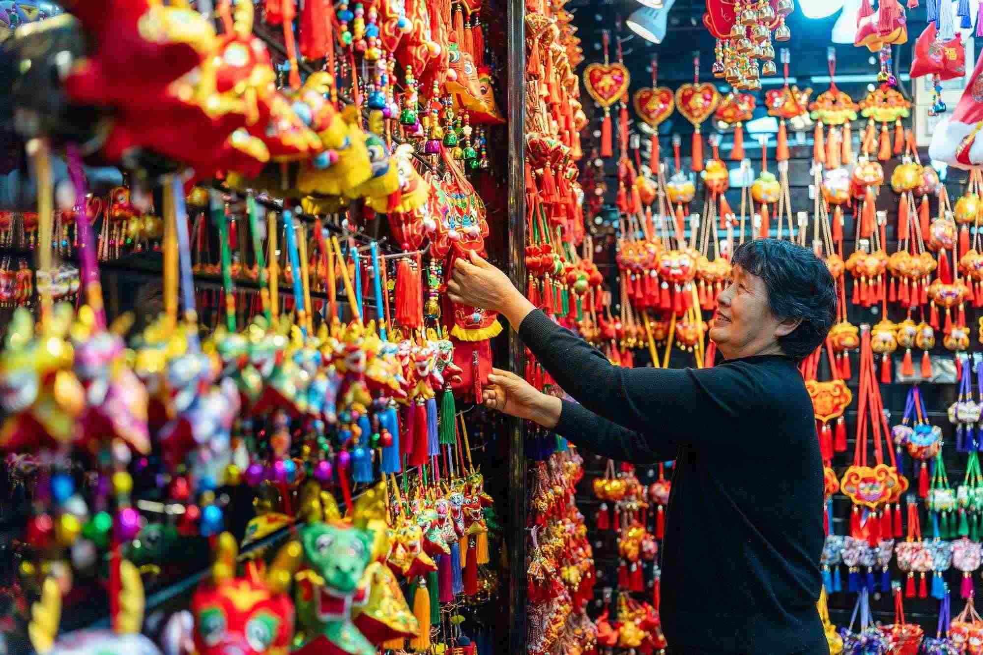 2023年12月11日，金華義烏國際商貿(mào)城，龍年喜慶用品掛滿攤位，顧客正在挑選中。