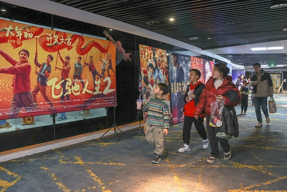 △ 2024年2月16日，在江西贛州一家電影院，觀眾從春節(jié)檔電影的宣傳展板前走過。