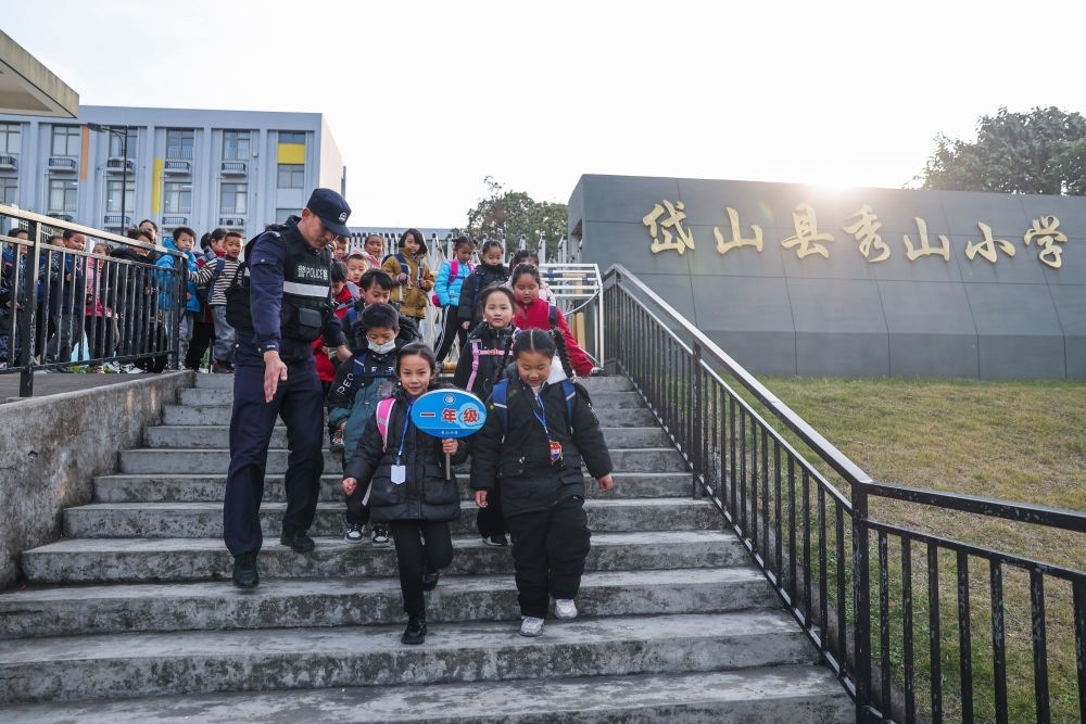 2023年12月20日，秀山派出所民警在秀山小學(xué)放學(xué)時(shí)間參與“護(hù)學(xué)崗”維持秩序，同時(shí)接獨(dú)自放學(xué)的學(xué)生去“民生小鋪”。浙江省舟山市岱山縣公安局秀山派出所聯(lián)合鄉(xiāng)鎮(zhèn)、社區(qū)成立“民生小鋪”，為當(dāng)?shù)鼐用瘛⑼鈦韯?wù)工人員及其子女等服務(wù)，協(xié)助解決外來務(wù)工人員在工作、生活等方面的矛盾和問題，助力鄉(xiāng)鎮(zhèn)基層治理。新華社記者 徐昱 攝