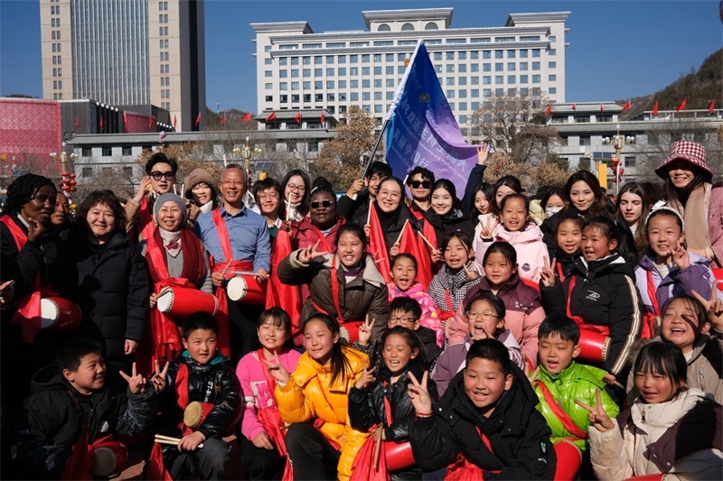 中外青年學(xué)子在安塞文化廣場觀看陜北腰鼓和大秧歌表演后合影留念，大家踏著鼓點(diǎn)共舞，翻飛的紅綢與躍動的身影交織，在黃土地廣場上繪出一幅生動的陜北民俗互動畫卷